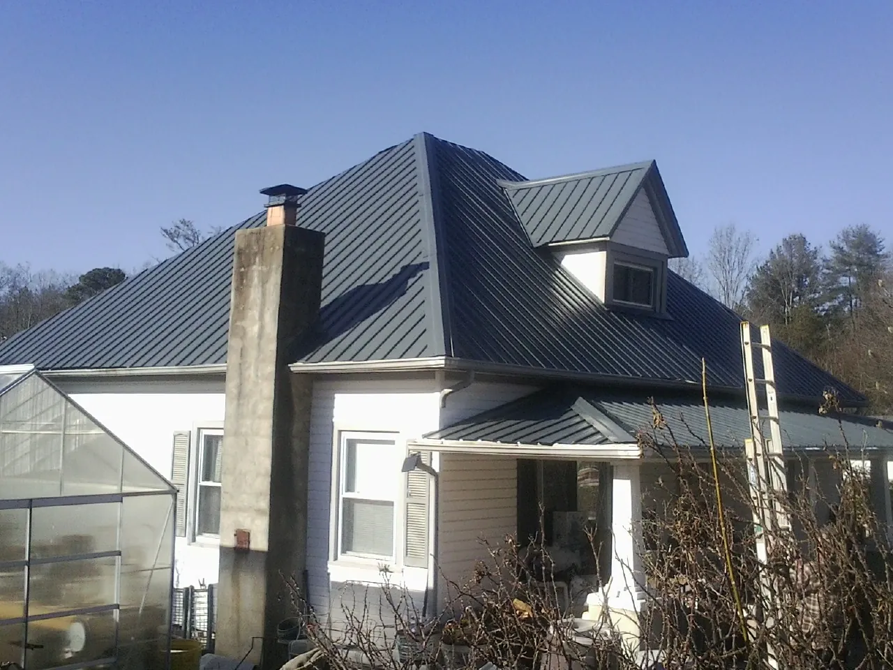 Dark blue standing seam metal roof on a white farmhouse with dormer — Slate & Tile Roof Repair by Roofing Brothers in West Point
