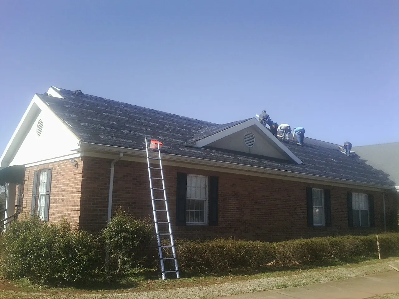 Crew tearing shingles off a brick ranch roof with a ladder set — Metal Roof Repair work by our crew in West Point